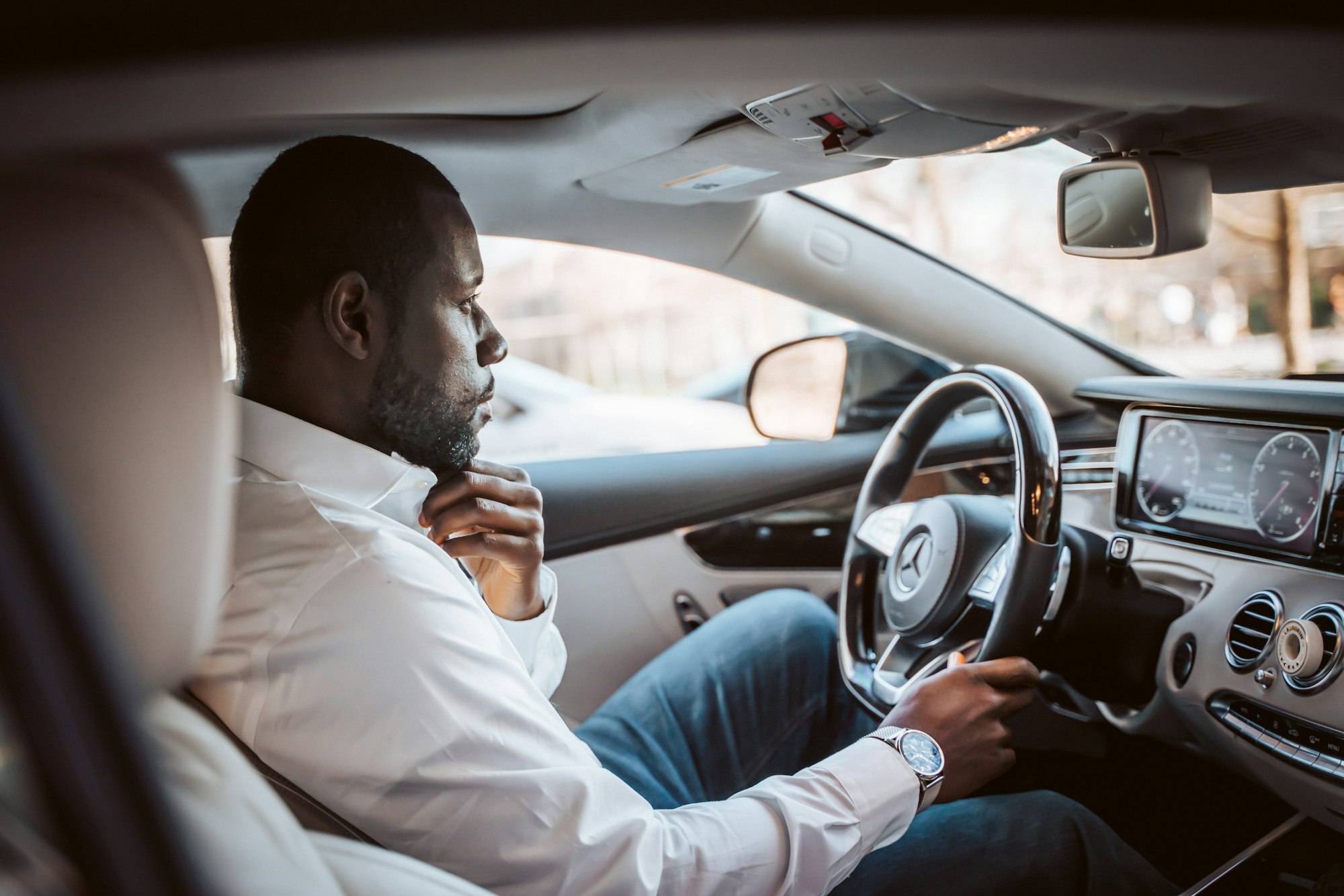 A driver in a white shirt at the wheel of a luxury car
